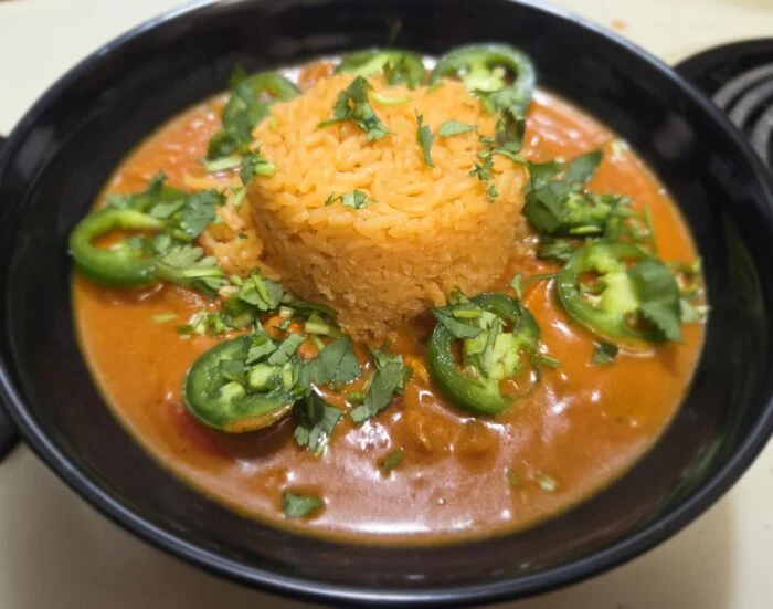 HelloFresh Brazilian style coconut chicken stew with a mound of rice, sliced jalapenos and cilantro in a black bowl