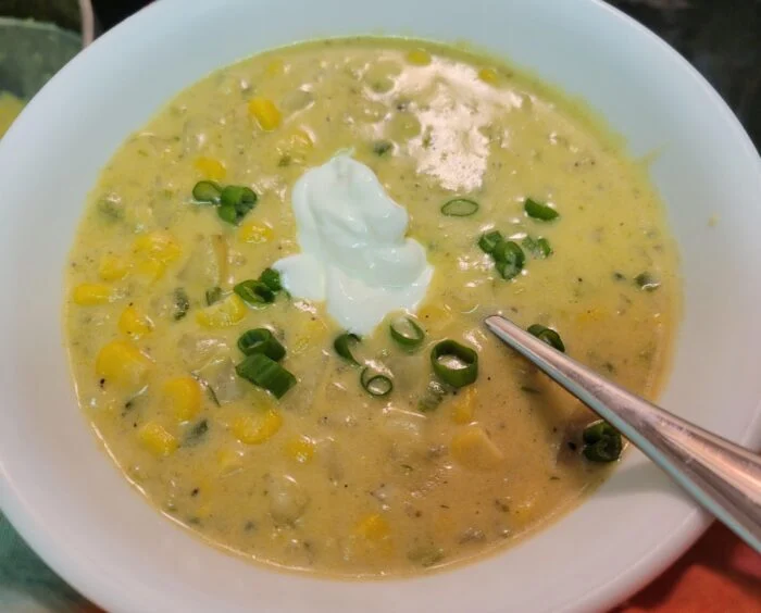 HelloFresh sweet corn and green pepper chowder topped with sour cream and scallions in a white bowl with a spoon