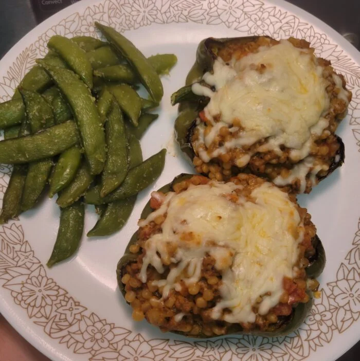 HelloFresh Tuscan beef stuffed peppers with pearled couscous and melted mozzarella beside snap peas on a floral plate