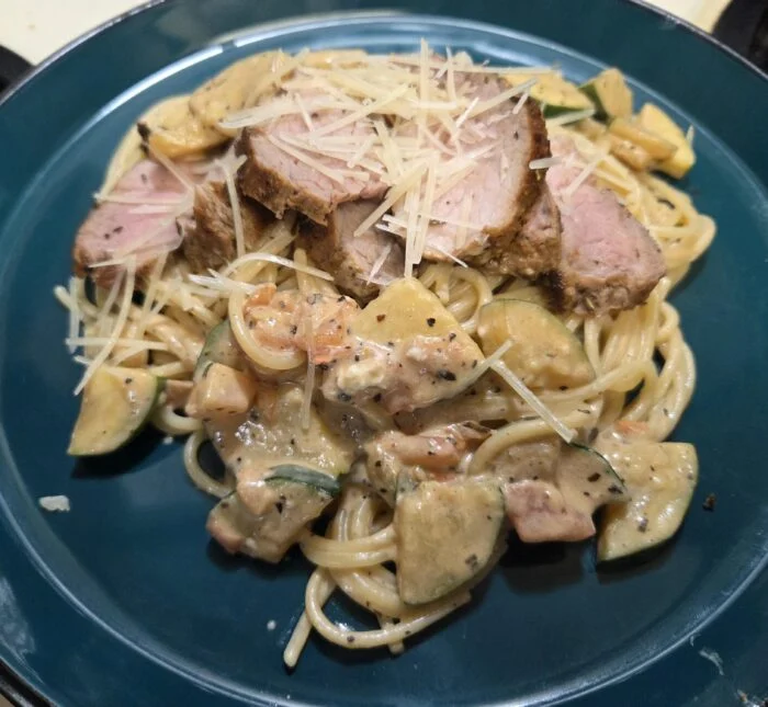 HelloFresh sliced Tuscan pork filet over creamy tomato spaghetti with zucchini and Parmesan on a teal plate