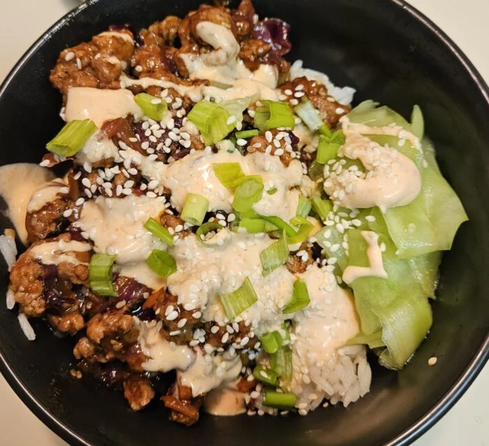 HelloFresh umami ginger pork over white rice with sriracha crema, scallions, sesame seeds and pickled cucumbers