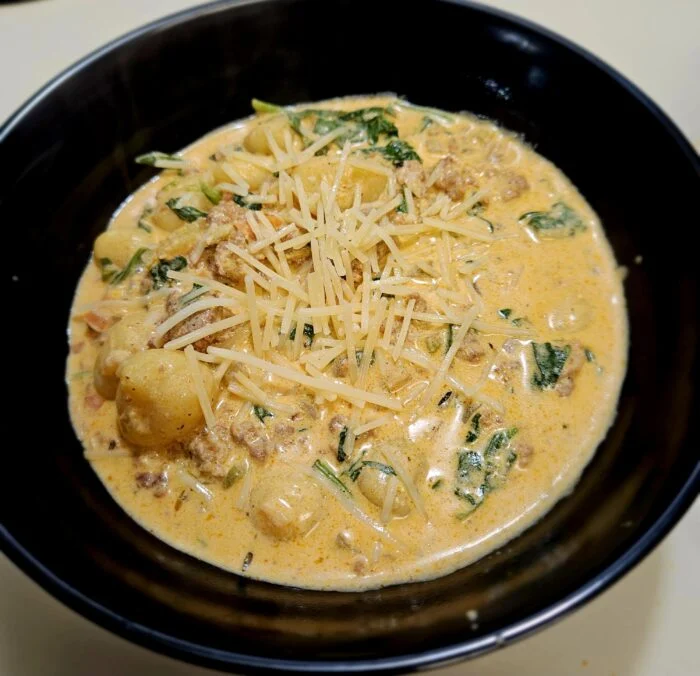 Home Chef sausage and gnocchi soup with spinach and shredded Parmesan in a black bowl