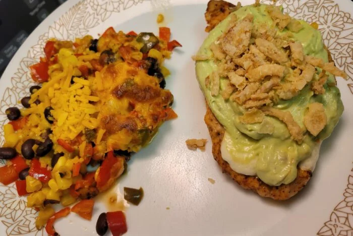 Home Chef guacamole crema chicken topped with crispy onions beside black bean, corn and pepper succotash on a floral plate
