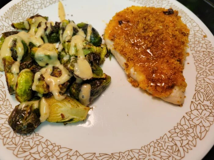 Home Chef hot honey crispy chicken breast with roasted Brussels sprouts drizzled in sweet dijon sauce on a floral plate