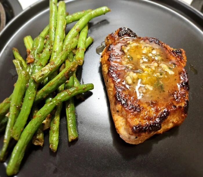 Home Chef peach and thyme glazed pork chop with garlic herb green beans on a dark plate