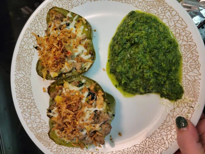 Home Chef spinach and artichoke turkey stuffed pepper halves with cheese and crispy onions, side of cooked greens on a plate
