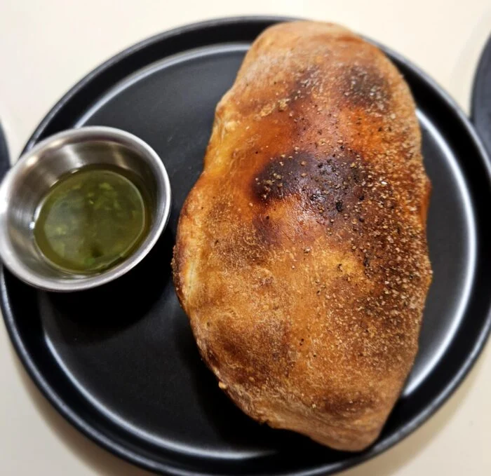 Marley Spoon beef picadillo pocket, a golden baked turnover on a black plate beside a cup of cilantro chimichurri