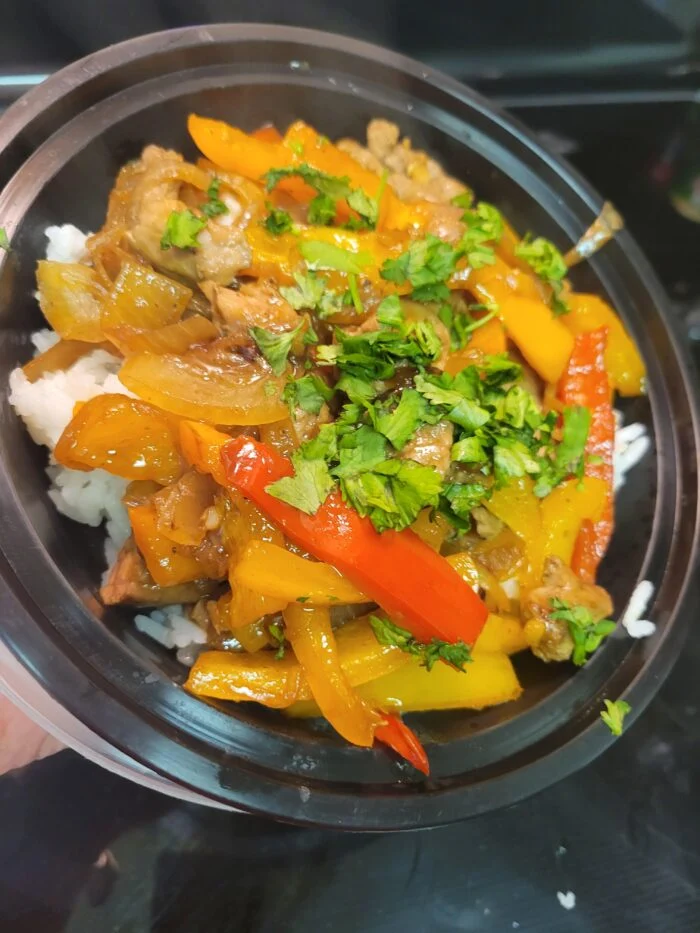 Marley Spoon Chinese pepper steak with red, yellow and orange peppers, onions and cilantro over white rice in a black bowl