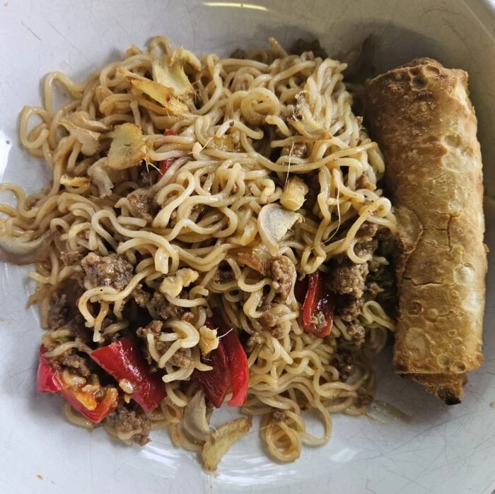 Marley Spoon ginger chili beef with stir fried ramen noodles and red peppers, served with an egg roll on a plate