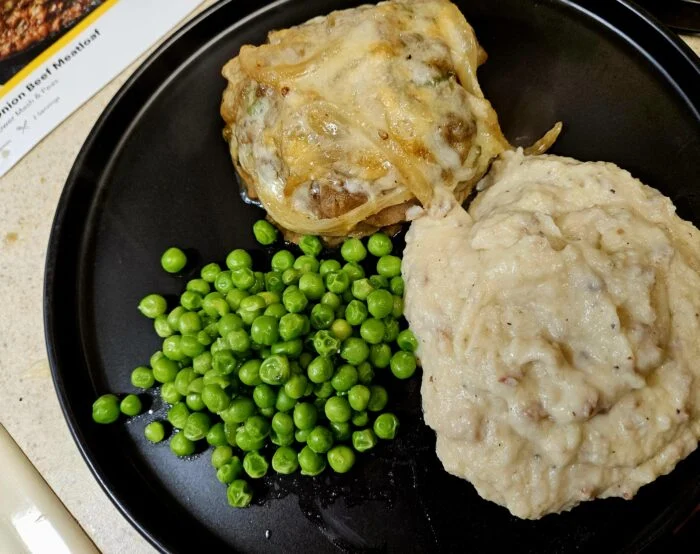 Marley Spoon French onion beef meatloaf topped with melted cheese, cauliflower mash and peas on a black plate