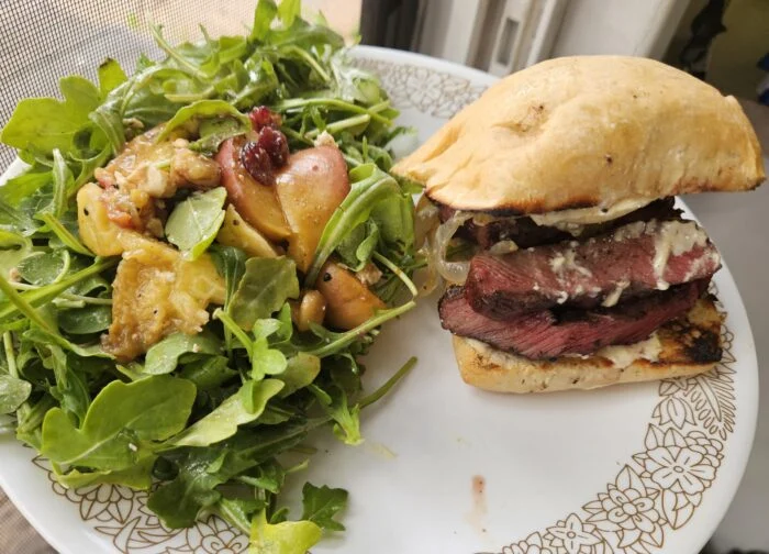 Marley Spoon grilled steak sandwich on a ciabatta roll with arugula salad and grilled peaches on a white plate