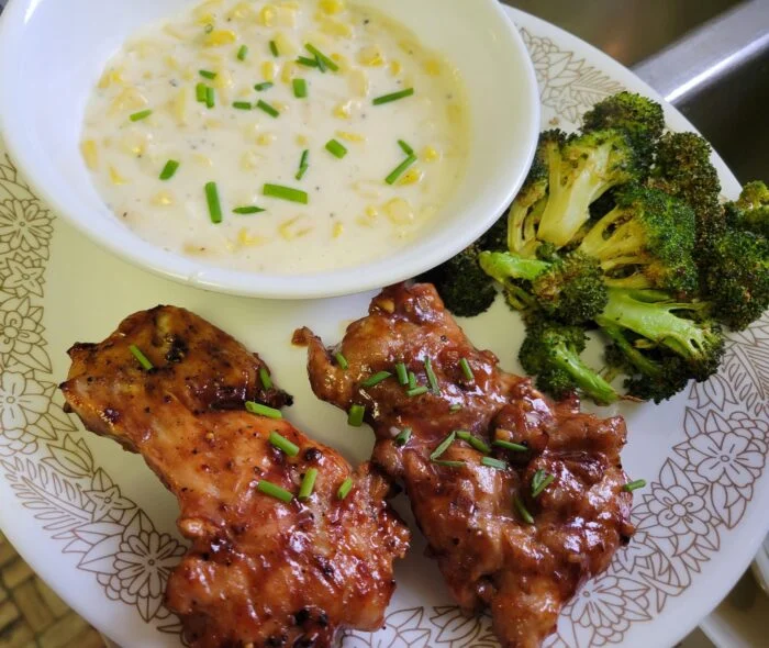 Marley Spoon honey BBQ chicken thighs with chives, roasted broccoli and a bowl of creamed corn on a plate