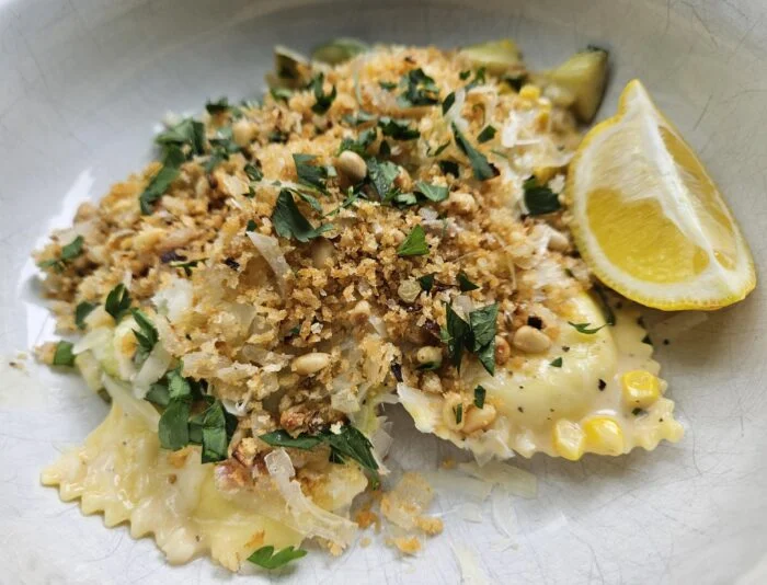 Marley Spoon lemon burrata ravioli with corn, zucchini, pine nut crumble, parsley and a lemon wedge in a white bowl