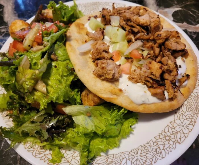 Marley Spoon pulled pork souvlaki on flatbread with tzatziki, cucumber and onion beside a Greek salad on a floral plate