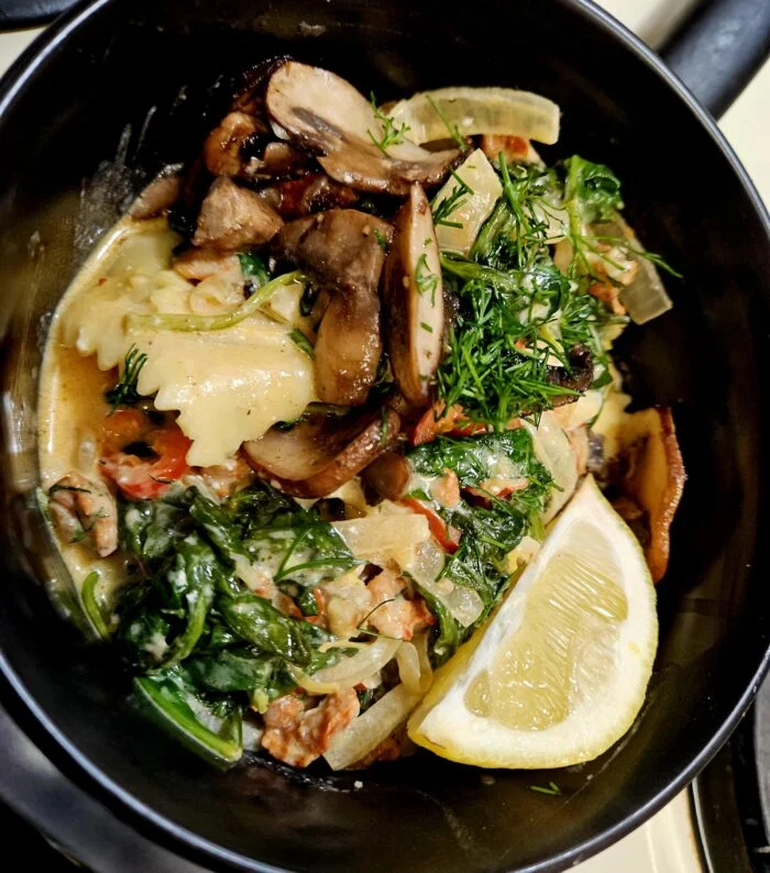 Marley Spoon beef ravioli in cream sauce with mushrooms, spinach, fresh dill and a lemon wedge in a dark pan