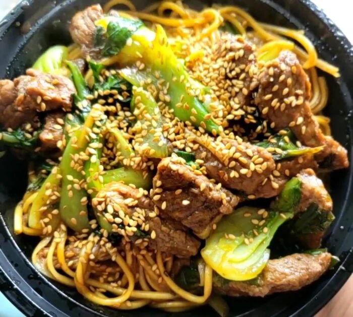 Marley Spoon Shanghai noodles with sirloin steak strips, bok choy and sesame seeds in a black bowl