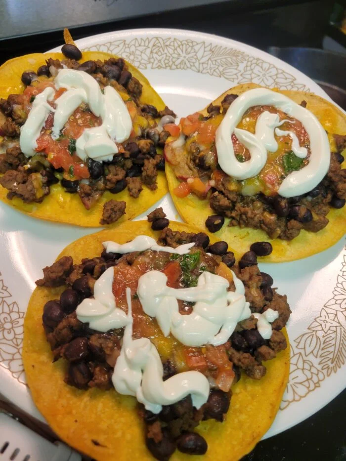 Marley Spoon smoky beef and black bean tostadas with salsa, melted cheese and sour cream drizzle on a floral plate