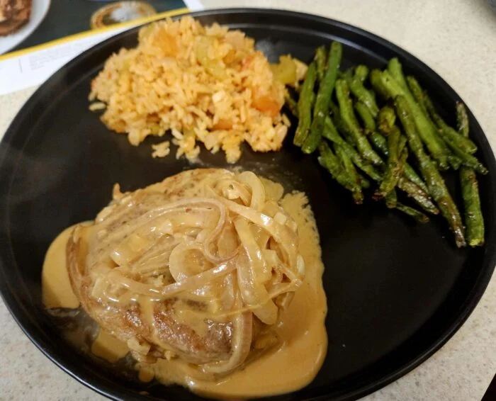 Marley Spoon smothered pork chop with creamy onion gravy, Creole rice and green beans on a black plate