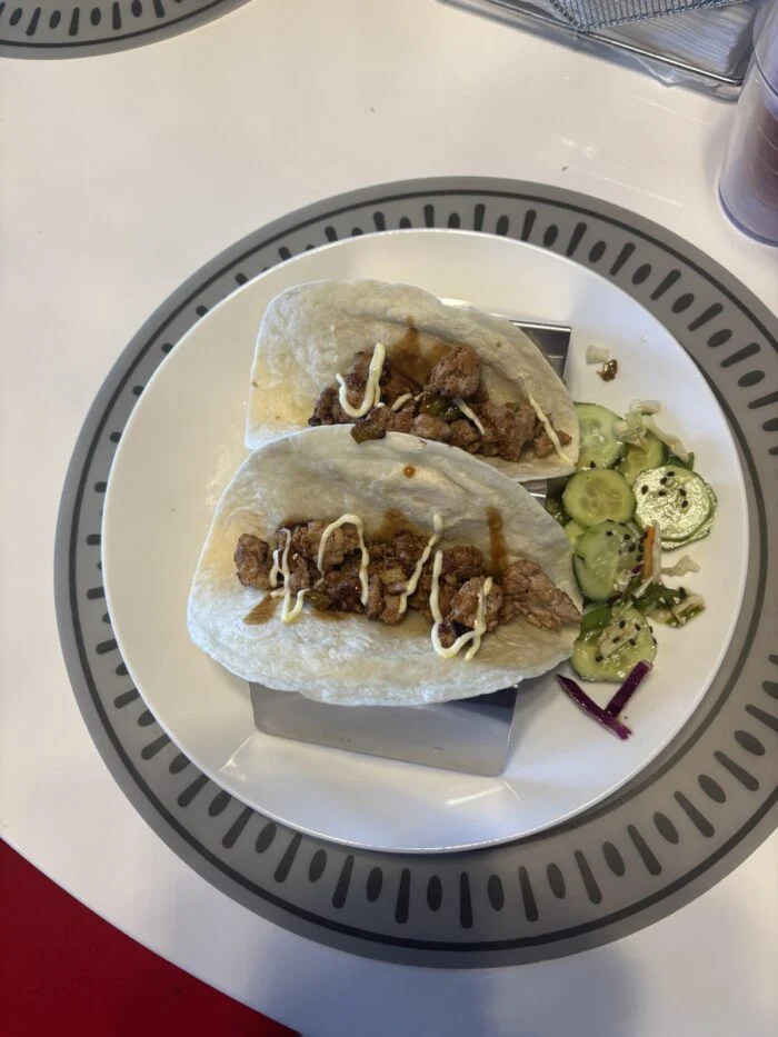 Home Chef pork tacos on a grey plate, two soft tortillas with drizzled sauce beside sliced cucumber