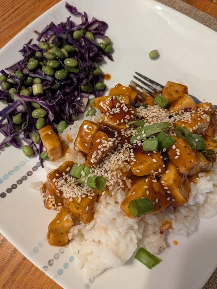 HelloFresh orange soy tofu cubes over white rice with shredded red cabbage and edamame on a white plate