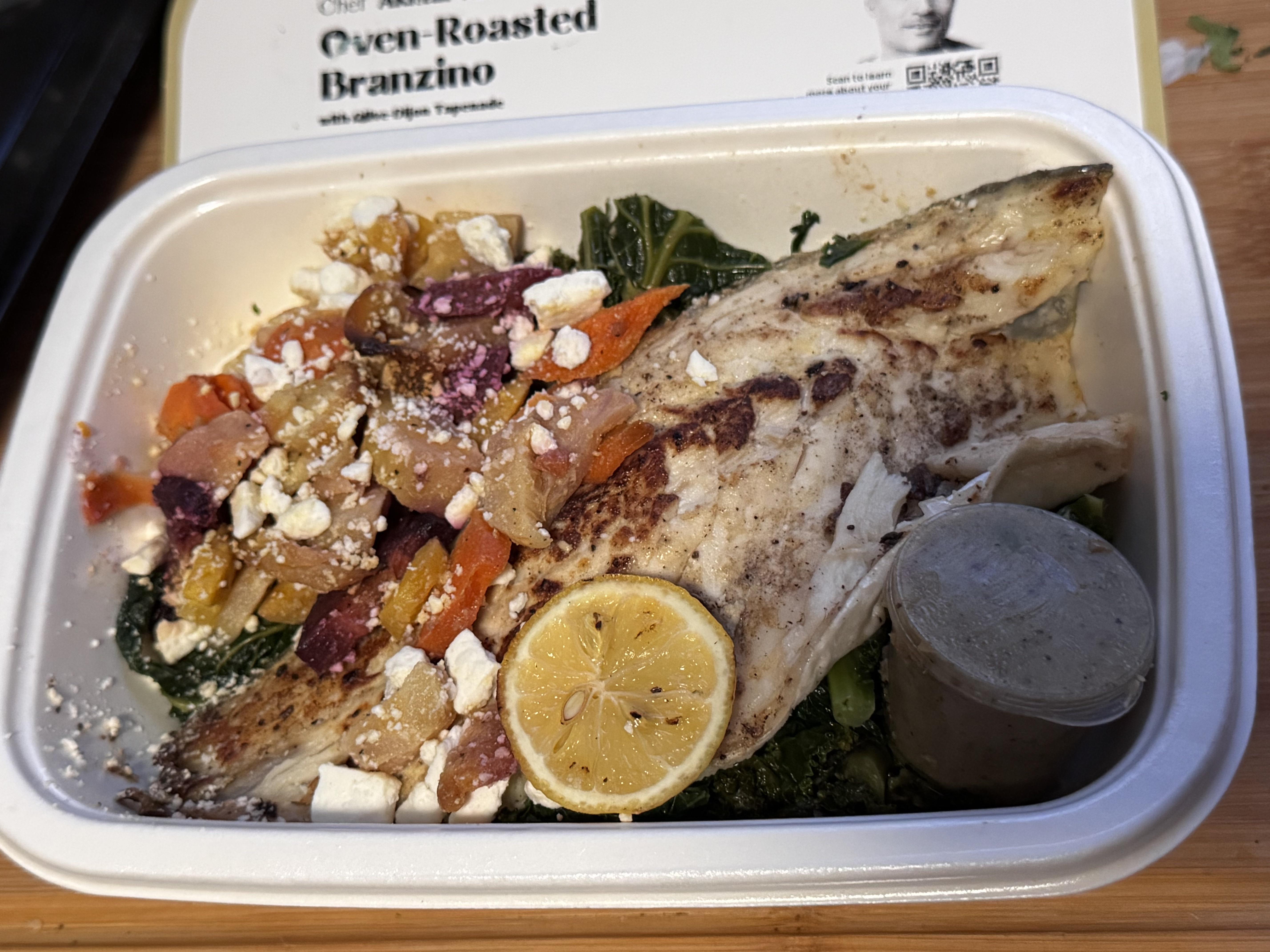 CookUnity oven roasted branzino with feta, peppers and greens, packaging sleeve behind the tray