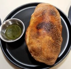 Marley Spoon beef picadillo pocket, a golden baked turnover on a black plate beside a cup of cilantro chimichurri