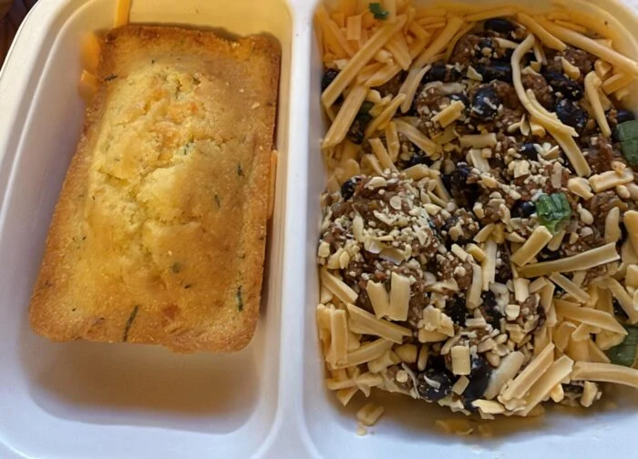 Reader photo of CookUnity beef and black bean chili topped with cheddar beside a corn muffin in its delivery tray