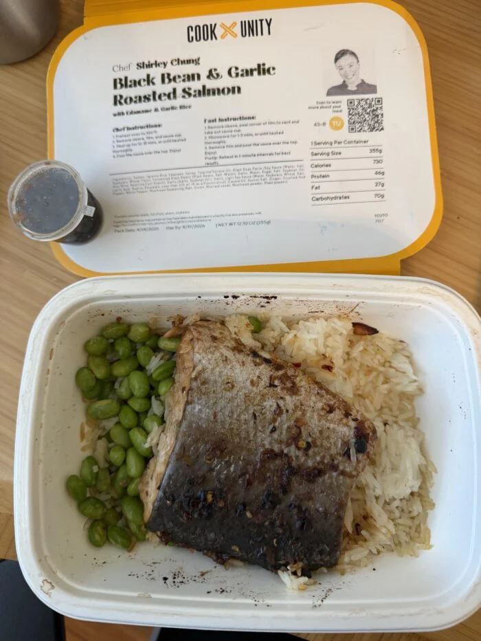 CookUnity black bean and garlic roasted salmon over rice with edamame in the tray, chef label behind