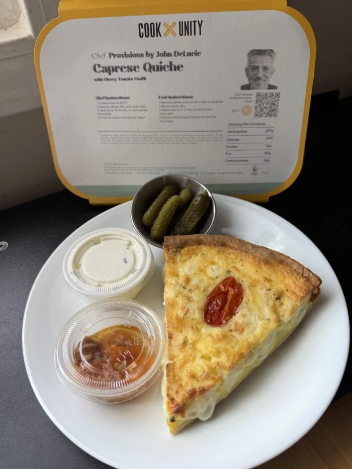 CookUnity caprese quiche slice on a white plate with cornichons and two sauce cups, chef label behind