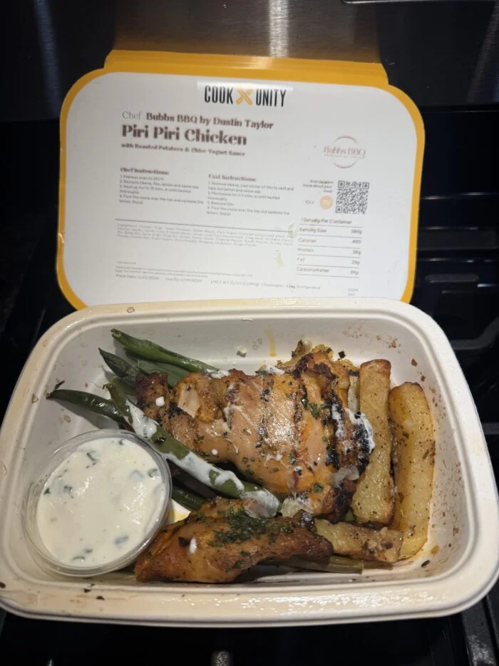CookUnity piri piri chicken with roasted potatoes, green beans and a sauce cup in its tray.