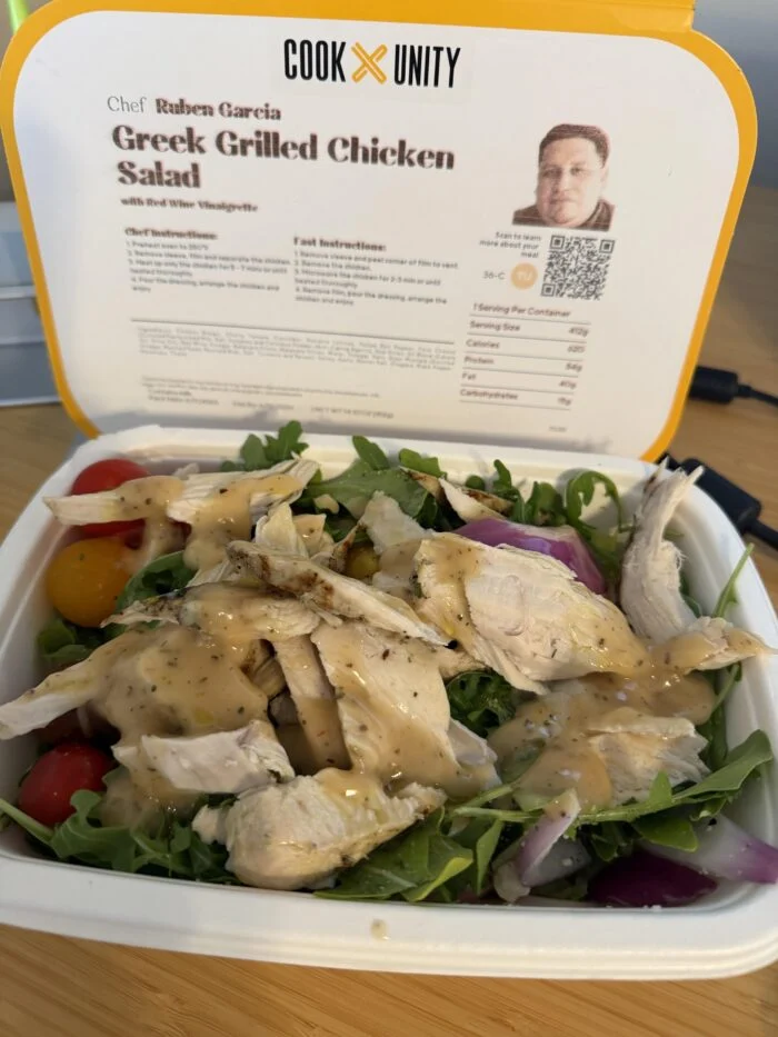 CookUnity Greek grilled chicken salad with greens, tomatoes and red onion in the tray, chef label behind