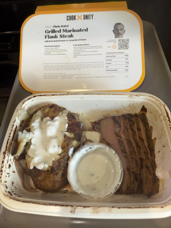 CookUnity grilled flank steak slices with a baked potato and a sauce cup in the tray, chef label behind