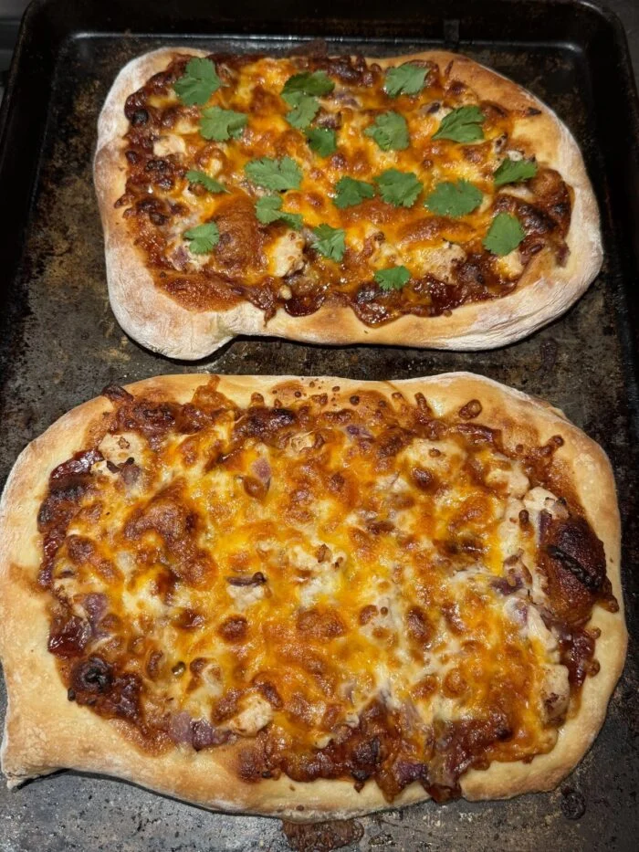 Two HelloFresh BBQ chicken flatbread pizzas with melted cheddar, red onion and cilantro on a baking sheet