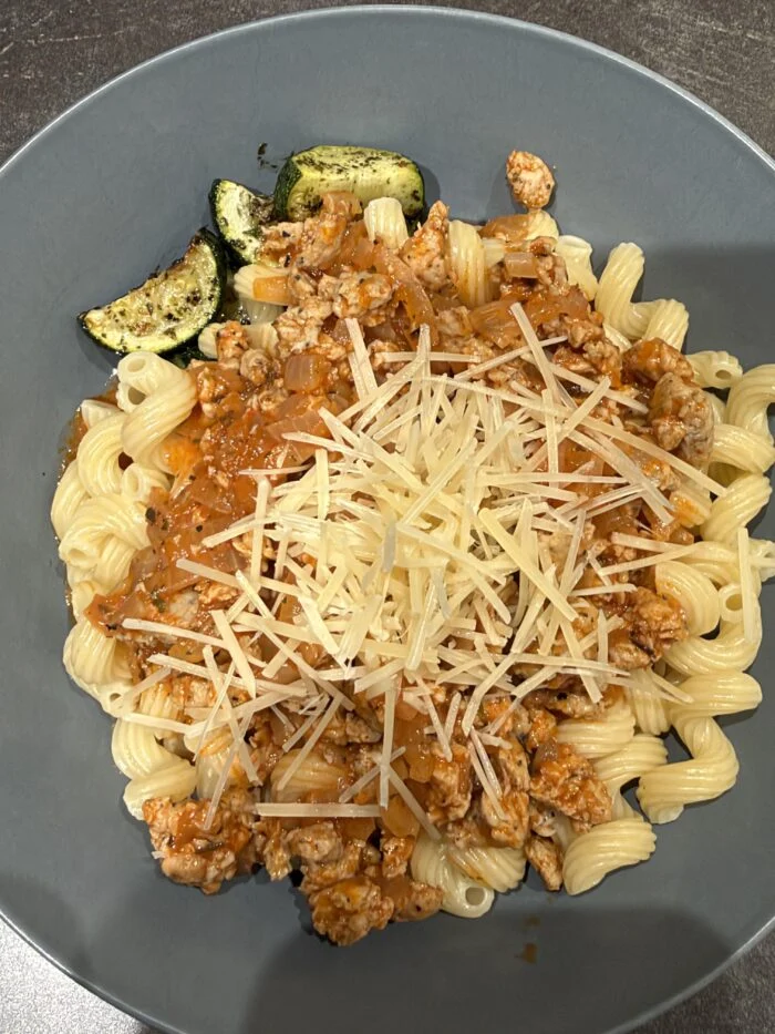 Reader-prepared HelloFresh chicken sausage cavatappi bolognese with grated cheese and zucchini on the plate.